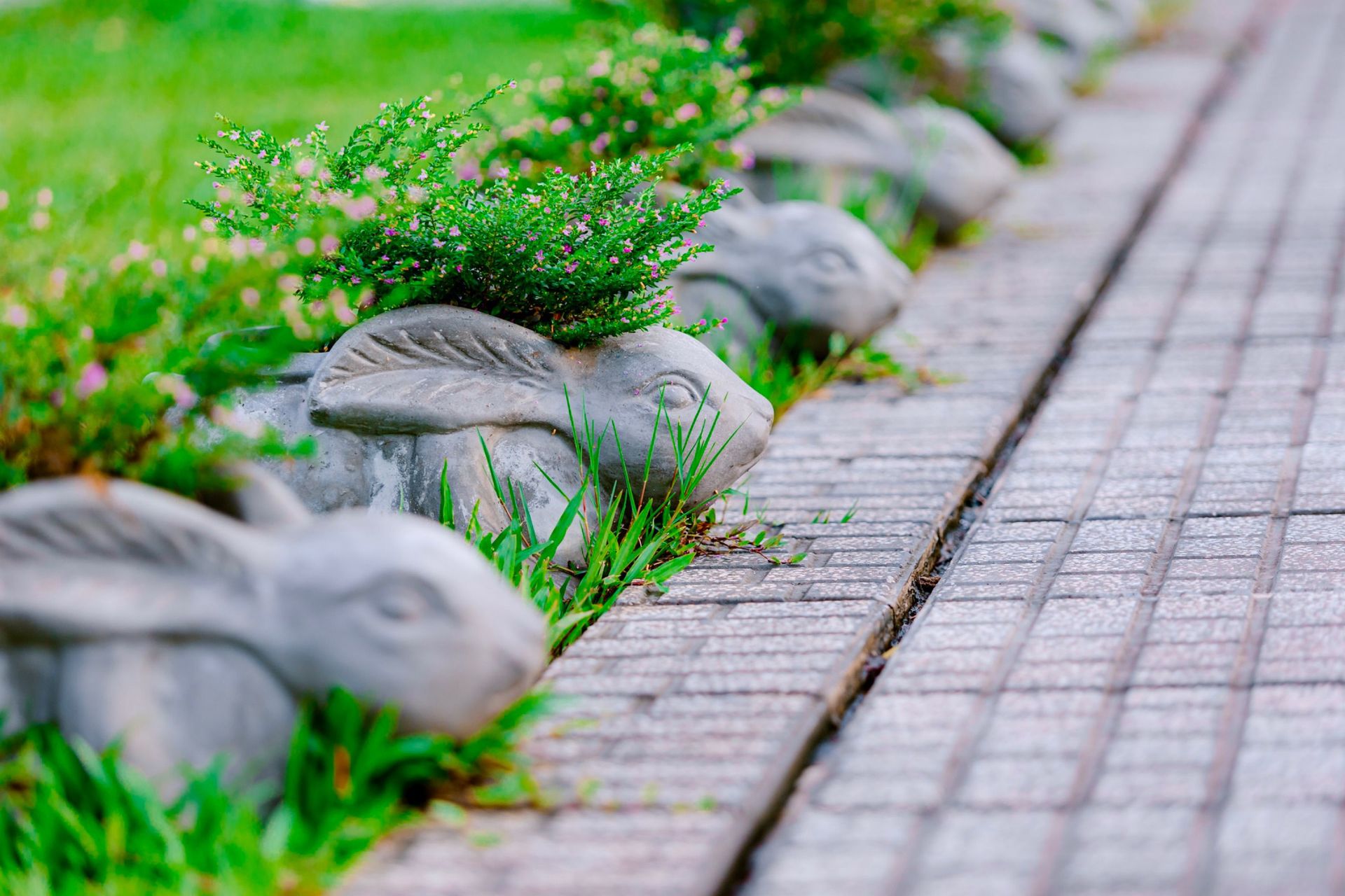 Concrete rabbit planters with flowers line a brick pathway in a vibrant garden setting.